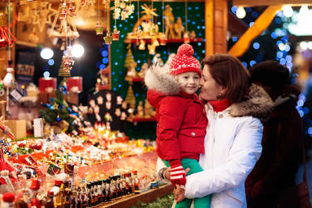 Mother and child in warm hat watching handmade glass Christmas tree ornaments at traditional German Xmas street market. Family with child shopping for Christmas presents on winter fair on snowy day.の写真素材