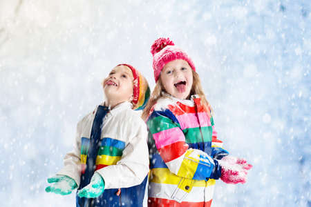 Kids playing in snow. Children play outdoors on snowy winter day. Boy and girl catching snowflakes in snowfall storm. Brother and sister throwing snow balls. Family Christmas vacation activity.の写真素材
