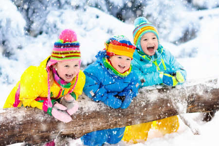 Kids playing in snow. Children play outdoors on snowy winter day. Boy and girl catching snowflakes in snowfall storm. Brother and sister throwing snow balls. Family Christmas vacation activity.の写真素材