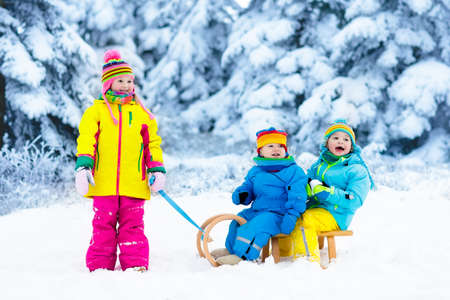 Little girl and boy enjoy a sleigh ride. Child sledding. Toddler kid riding a sledge. Children play outdoors in snow. Kids sled in Alps mountains in winter. Outdoor fun for family Christmas vacation.の写真素材