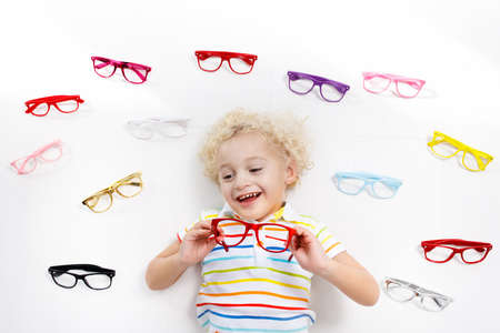 Child at eye sight test. Little kid selecting glasses at optician store. Eyesight measurement for...