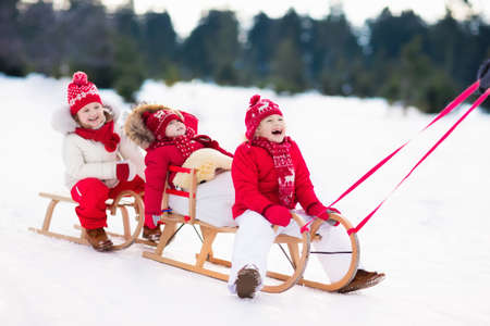 Little girl and boy enjoy a sleigh ride. Child sledding. Toddler kid riding a sledge. Children play...