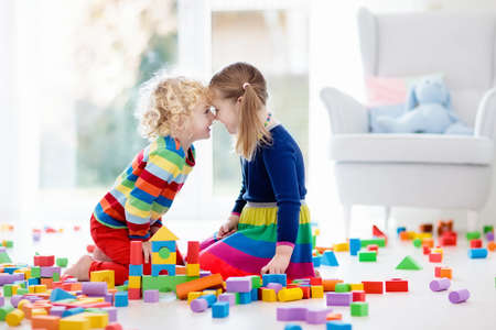 Kids play with wooden toy blocks. Educational colorful toys for children. Boy and girl playing in kindergarten room with big window. Kid building tower with rainbow blocks. Child at home.の写真素材