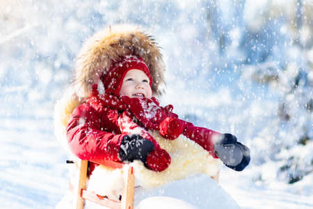 Sled and snow fun for kids. Baby sledding in snowy winter park. Little boy in warm red jacket and...