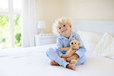 Kids playing in parents bed. Children wake up in sunny white bedroom. Little boy in bllue pajamas. Sleepwear and bedding for child and baby. Nursery interior for toddler kid. Family morning.の写真素材