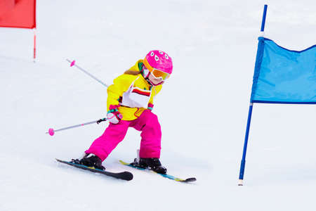 Child skiing in mountains. Active toddler kid with safety helmet, goggles and poles. Ski race for young children. Winter sport for family. Kids ski lesson in alpine school. Little skier racing in snowの写真素材