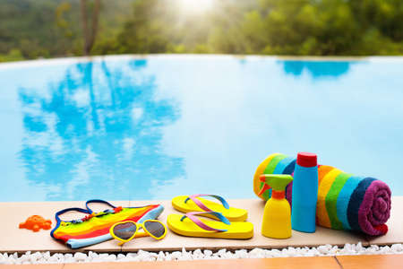 Swimming pool accessories flat lay. Top view of beach items on pool deck. Flip flops, bikini and hat, sun glasses. Water toys. Summer vacation in tropical resort. Copy space. Colorful beach wear.の写真素材