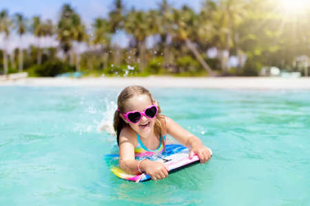 Child surfing on tropical beach. Family summer vacation in Asia. Kids swim in ocean water. Kid on surf body board. Little girl swimming in exotic sea. Travel with children. Water and beach sport.の写真素材