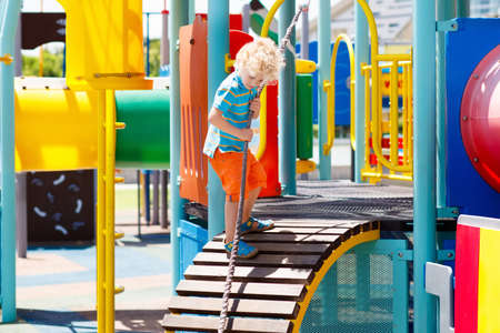 Kids climbing and sliding on outdoor playground. Children play in sunny summer park. Activity and amusement center in kindergarten or school yard. Child on colorful slide. Toddler kid outdoors.の写真素材