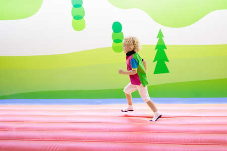 Child jumping on colorful playground trampoline. Kids jump in inflatable bounce castle on kindergarten birthday party. Activity and play center for young child. Little boy playing indoors.の写真素材