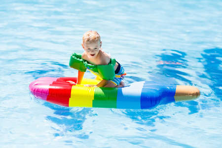 Happy child on inflatable ice cream float in outdoor swimming pool of tropical resort. Summer...