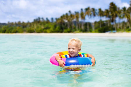 Child with inflatable ring on beautiful beach. Little boy swimming in exotic sea. Ocean vacation...