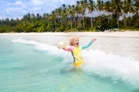 Child on beautiful beach. Little boy with toy boat running and jumping at sea shore. Ocean vacation with kid. Children play on summer beach. Water fun. Kids swim. Family holiday on tropical island.の写真素材