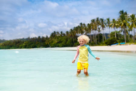 Child on beautiful beach. Little boy with toy boat running and jumping at sea shore. Ocean vacation with kid. Children play on summer beach. Water fun. Kids swim. Family holiday on tropical island.の写真素材