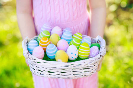 Easter egg hunt. Little girl with eggs basket. Kids searching for sweets and chocolate on Easter morning in garden. Child with spring pastel decoration.  Kid in pink dress with painted eggs.の写真素材