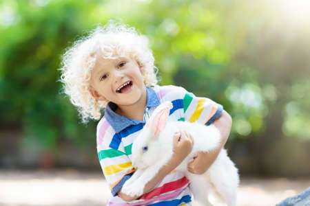 Child playing with white rabbit. Little boy feeding and petting white bunny. Easter celebration. Egg hunt with kid and pet animal. Children and animals. Kids take care of pets. Spring Easter garden.の写真素材
