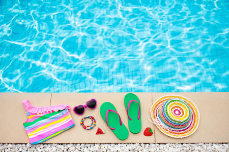 Swimming pool accessories flat lay. Top view of beach items on pool deck. Flip flops, bikini and hat, sun glasses. Water toys. Summer vacation in tropical resort. Copy space. Colorful beach wear.の写真素材