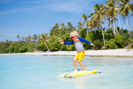 Little boy surfing on a tropical beach in Asia. Child on surf board on ocean wave. Active water sports for kids. Kid swimming with body board. Young surfer in exotic sea. Swim and eye wear for kids.の写真素材