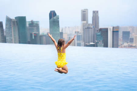 Children swimming in roof top outdoor pool on family vacation in Singapore. City skyline from...
