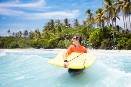 Teenager boy surfing on tropical beach in Asia. Child on surf board on ocean wave. Active water...