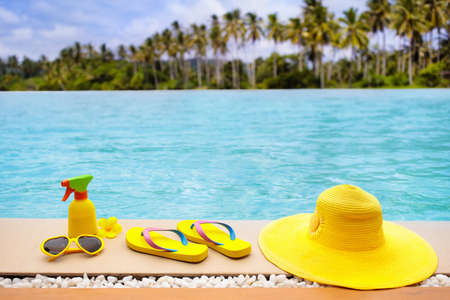 Swimming pool accessories flat lay. Top view of beach items on infinity pool deck. Flip flops, bikini and hat, sun glasses. Water toys. Summer vacation in tropical resort. Copy space. Colorful beach wear.の写真素材