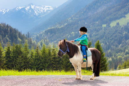 Kid riding pony in the Alps mountains. Family spring vacation on horse ranch in Austria, Tirol.の写真素材