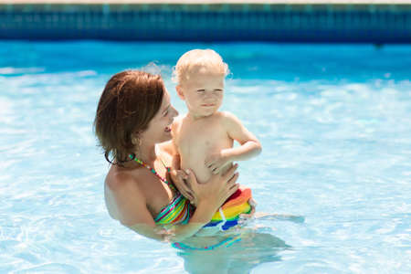 Mother and baby in outdoor swimming pool of tropical resort. Kid learning to swim. Mom and child playing in water. Family summer vacation in exotic destination. Active and healthy sport for kids.の写真素材