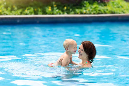 Mother and baby in outdoor swimming pool of tropical resort. Kid learning to swim. Mom and child...