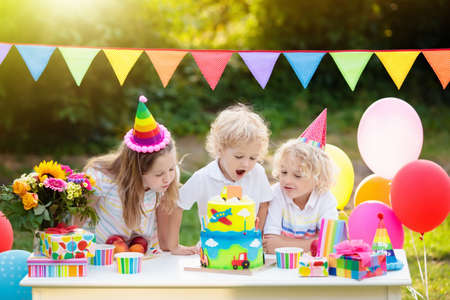 Children blow candles on birthday cake. Kids party decoration and food. Boy and girl celebrating...