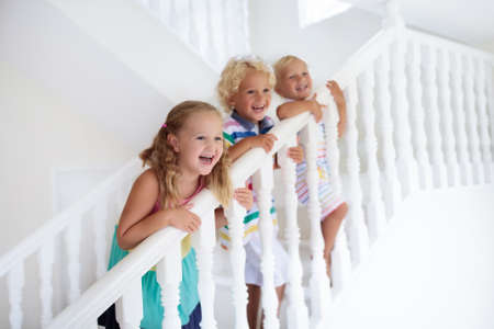 Kids walking stairs in white house. Children playing in sunny staircase. Family moving into new home. Boy and girl on steps of modern stairway. Foyer and living room interior. Child at stair case.の写真素材