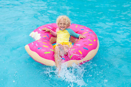 Child in a swimming pool on a funny inflatable donut float ring. Little boy learning to swim in an...