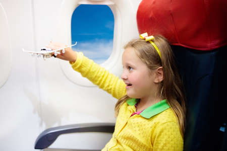 Child in airplane. Kid in air plane sitting in window seat. Flight entertainment for kids. Traveling with young children. Kids fly and travel. Family summer vacation. Little girl with toy in airplaneの写真素材