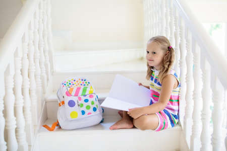 Kid walking stairs in white house. Little girl playing in sunny staircase. Child reading book or...