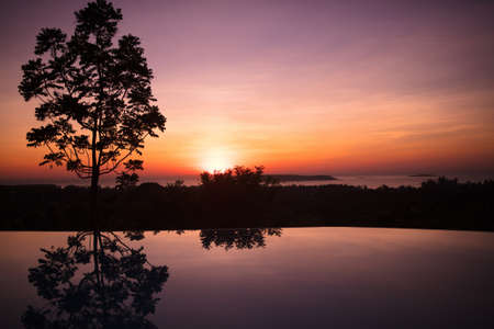 Infinity pool of tropical resort at sunset. Sun reflection in water of outdoor swimming pool on a beach in Asia. Romantic evening location and setting. Sunrise at exotic sea.の写真素材