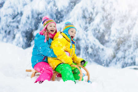 Little girl and boy enjoying sleigh ride. Child sledding. Toddler kid riding a sledge. Children play...