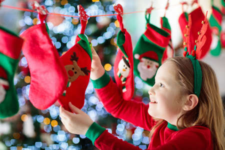 Kids opening Christmas presents. Child searching for candy and gifts in advent calendar on winter morning. Decorated Christmas tree for family with children. Little girl in Xmas pajamas.の写真素材