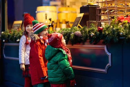 Children shopping on traditional Christmas market in Germany on snowy winter day. Kids buying waffle, candy, pastry and gingerbread in fair sweet shop. Boy and girl choosing sweets in Xmas bakery.の写真素材