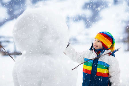 Child building snowman. Kids build snow man. Little boy playing outdoors on snowy winter day. Outdoor family fun on Christmas vacation. Little boy playing snow balls flight. Winter clothing active kidの写真素材