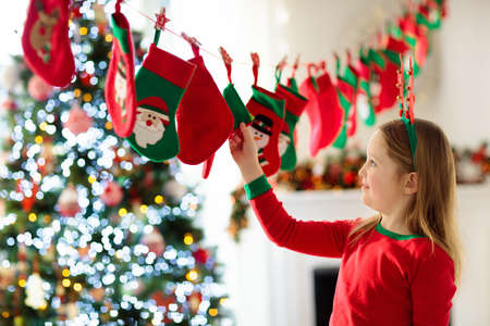 Kids opening Christmas presents. Child searching for candy and gifts in advent calendar on winter morning. Decorated Christmas tree for family with children. Little girl in Xmas pajamas.の写真素材