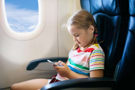 Child in airplane. Kid with mobile phone in air plane in window seat. Flight entertainment for kids....