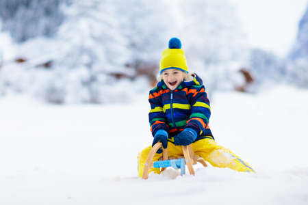 Little boy enjoying a sleigh ride. Child sledding. Toddler kid riding a sledge. Children play outdoors in snow. Kids sled in the Alps mountains in winter. Outdoor fun for family Christmas vacation.の写真素材