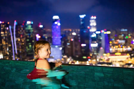Children swimming in roof top outdoor pool on family vacation in Singapore. City skyline from infinity pool in luxury hotel. Kids swim and enjoy skyscraper view in Asia. Travel with young child.の写真素材