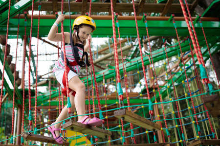 Child in forest adventure park. Kids climb on high rope trail. Agility and climbing outdoor...