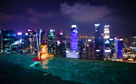 Children swimming in roof top outdoor pool on family vacation in Singapore. City skyline from infinity pool in luxury hotel. Kids swim and enjoy skyscraper view in Asia. Travel with young child.の写真素材