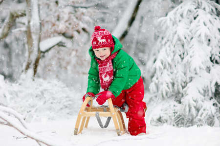 Little boy enjoying a sleigh ride. Child sledding. Toddler kid riding a sledge. Children play outdoors in snow. Kids sled in the Alps mountains in winter. Outdoor fun for family Christmas vacation.の写真素材