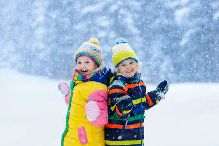 Kids playing in snow. Children play outdoors on snowy winter day. Boy and girl catching snowflakes in snowfall storm. Brother and sister throwing snow balls. Family Christmas vacation activity.の写真素材