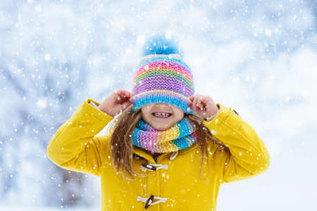 Child in knitted hat playing in snow on Christmas vacation. Winter outdoor fun. Knitting and outerwear for family. Kids play in snowy park. Little girl in knit scarf and mittens catching snowflakes.の写真素材