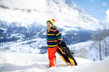 Little boy enjoying a sleigh ride. Child sledding. Toddler kid riding a sledge. Children play outdoors in snow. Kids sled in the Alps mountains in winter. Outdoor fun for family Christmas vacation.の写真素材