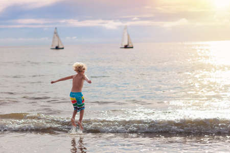 Child playing on ocean beach. Kid jumping in the waves at sunset. Sea vacation for family with kids. Little boy running on tropical beach of exotic island during summer holiday. Swim wear for childrenの写真素材