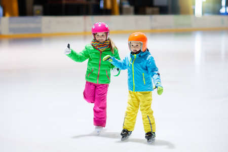 Child skating on indoor ice rink. Kids skate. Active family sport during winter vacation and cold season. Little girl and boy in colorful wear training or learning ice skating. School sport clubsの写真素材